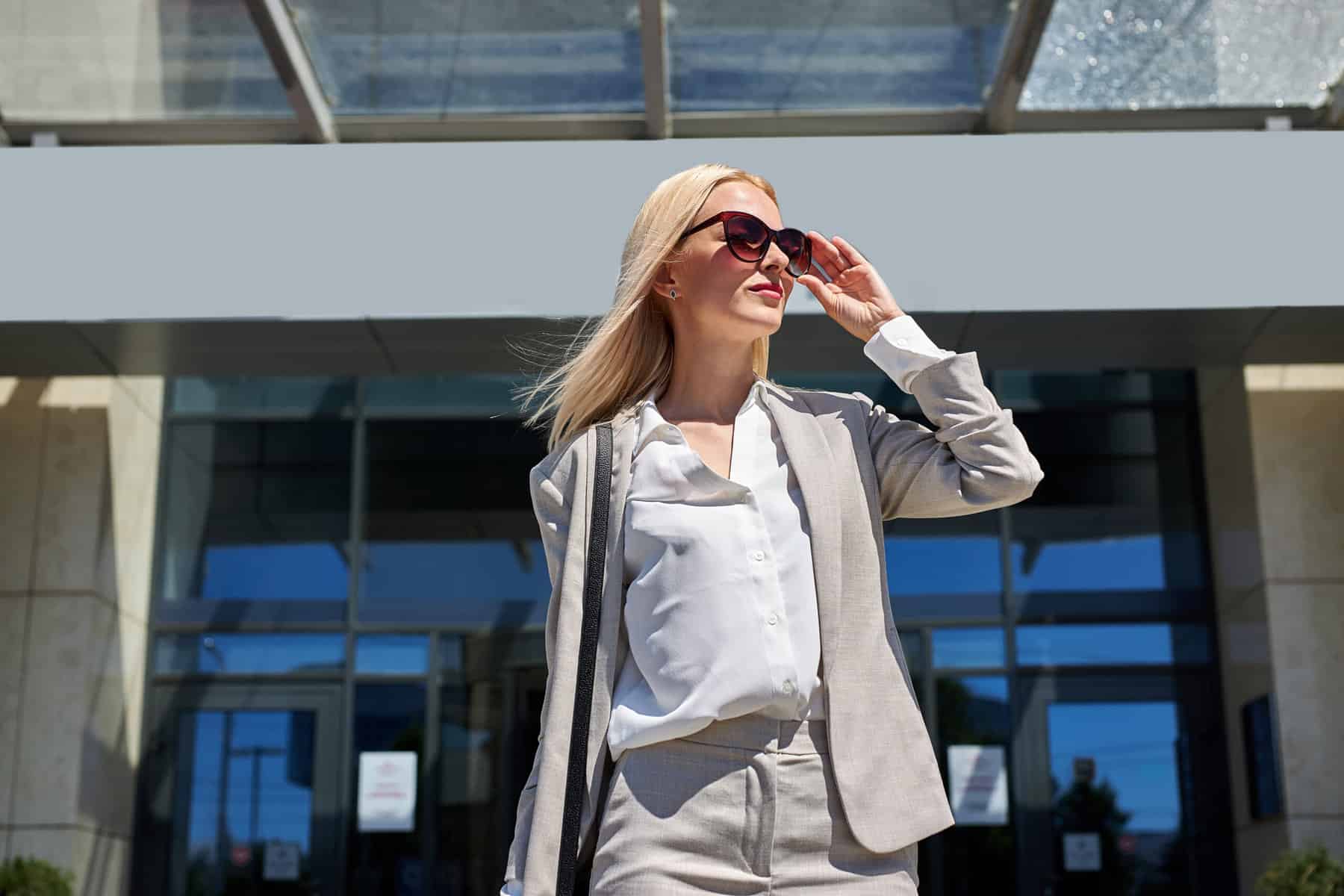 dress code airline successful businesswoman on business trip, young blonde lady looks away in search of taxi, next to luxurious hotel