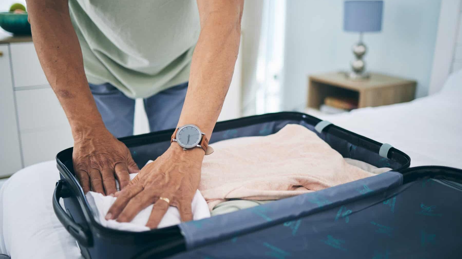 Man, hands and packing suitcase in home for travel, holiday trip and vacation. Closeup, person in bedroom and prepare clothes in luggage bag for journey, solo adventure and leaving for tourism voyage